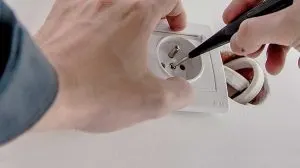 Electrician using tweezers to install a white power outlet