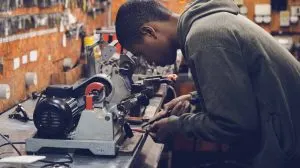Young electrician using a pipe-threading machine at a workshop bench full of tools