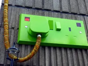 Oversized green plug and socket sculpture on a concrete wall
