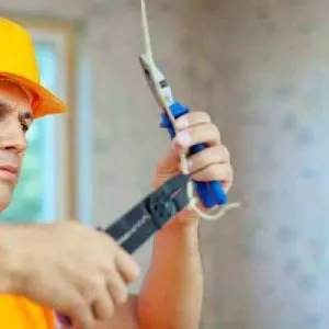 Electrician in hard hat using a crimping tool on wiring