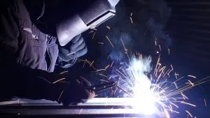 Welder in helmet and gloves welding steel with bright sparks flying