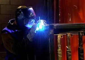 Welder in mask welding a metal railing frame with a bright blue arc