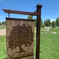 Hanging Muirwood sign with metal tree cutout on a decorative post outdoors