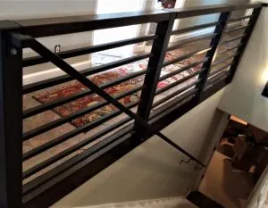 Dark horizontal-bar metal stair railing overlooking a lower level stairwell