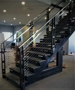 Modern black staircase with horizontal cable railing under construction indoors