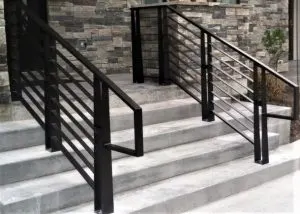 Black horizontal-bar metal handrail on stone exterior entry steps