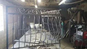 Ornamental wrought iron railing being fabricated on a welding table in a workshop