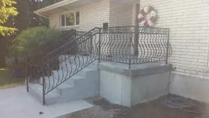 Ornate black wrought iron railing on concrete front porch steps of a brick home