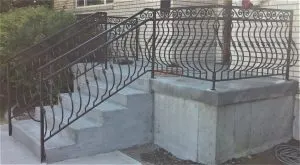 Custom scrollwork wrought iron railing along concrete steps and porch of a brick house