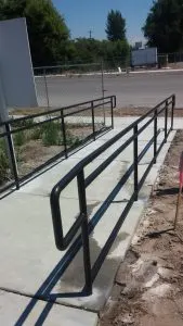 Black metal handrails lining a concrete wheelchair ramp outdoors