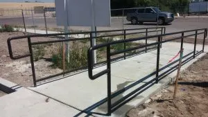 Black metal ADA handrails along a concrete accessibility ramp at a commercial site