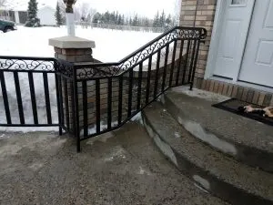 Black scrollwork metal railing along a curved concrete front entry ramp in winter