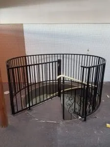 Curved black metal railing surrounding a spiral staircase opening, shop floor