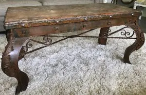 Rustic coffee table with a hammered copper top and scrolled wrought iron legs on a shag rug