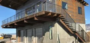 Horizontal-bar metal deck railing and open stairs on a steel-clad home over concrete garage bays