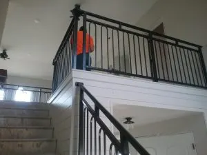 Worker in orange shirt installing a black metal loft railing above a staircase