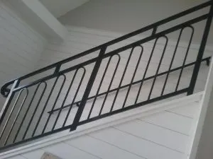 Black metal stair railing with rounded balusters against white shiplap walls