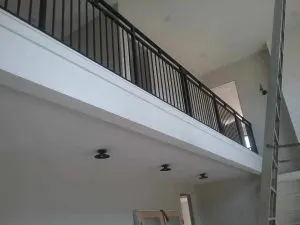 Black metal loft railing overlooking an interior room with recessed lighting