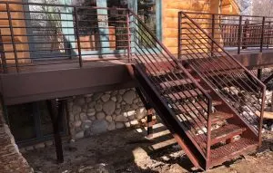 Rust-finished steel deck railing and open-riser stairs on a log-sided home