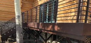 Brown metal deck railing along an elevated deck and stairs on a log cabin home