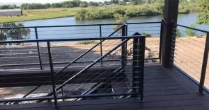 Modern black metal deck railing with horizontal bars and cable infill overlooking a river