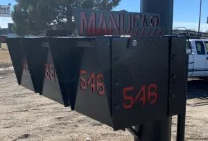 Custom black diamond-plate mailboxes with red cut-out address numbers and MANUFAB lettering outside the shop