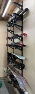 Wall-mounted metal rack holding skis and snowboards in a storage room