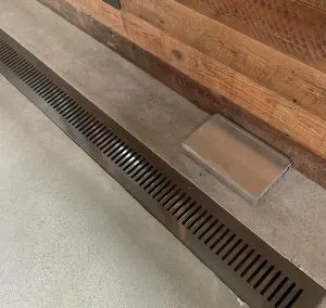 Metal floor grate drain and access cover set into a polished concrete floor by a wood wall