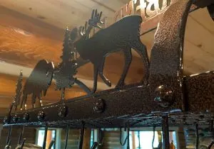 Metal pot rack detail showing cut-out elk and pine tree silhouettes below a wood ceiling