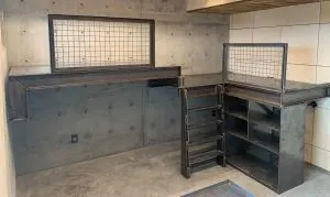 Custom steel countertop and shelving units built into a concrete-walled utility room