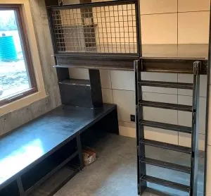 Custom steel workbench with mesh cabinet, shelving, and ladder-style storage in a concrete-walled room
