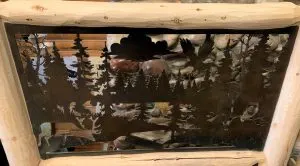 Metal panel with cut-out forest, eagle, and deer scene framed in log railing