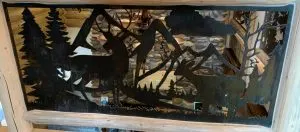 Metal railing panel with cut-out silhouette of deer in a mountain forest scene
