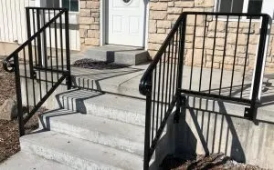 Black metal handrails flanking concrete steps at a stone home entrance