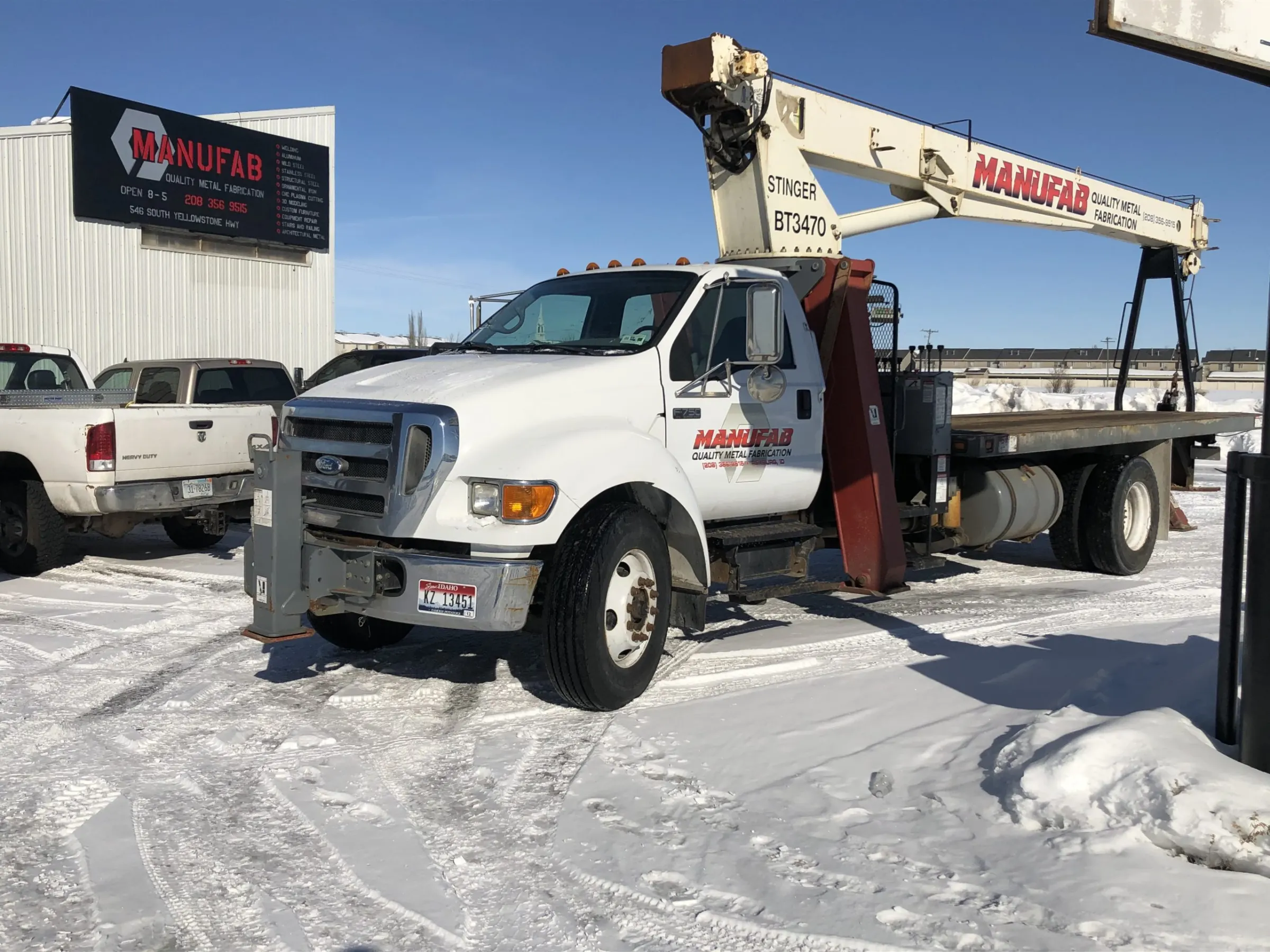 Manufab crane truck parked in snow outside the Manufab shop and sign