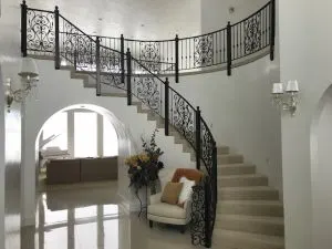 Curved staircase with ornate wrought-iron railing in a bright entryway